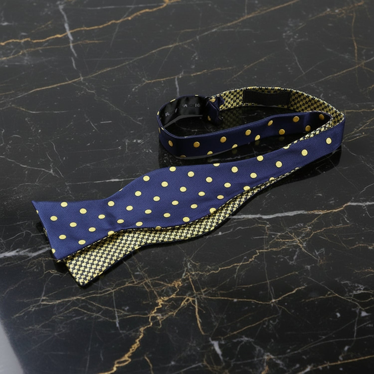 A double-sided self-tie bow tie with one side navy blue and gold dots pattern, and the other side yellow and blue stripes pattern.