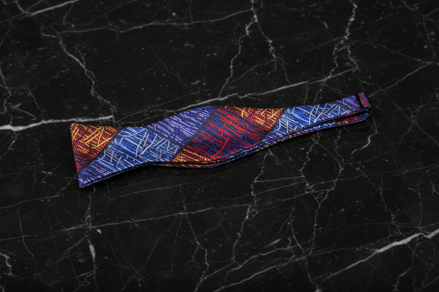 A self-tie bow tie and pocket square set with an abstract geometric pattern in blue, orange, and red colors displayed on a white background.