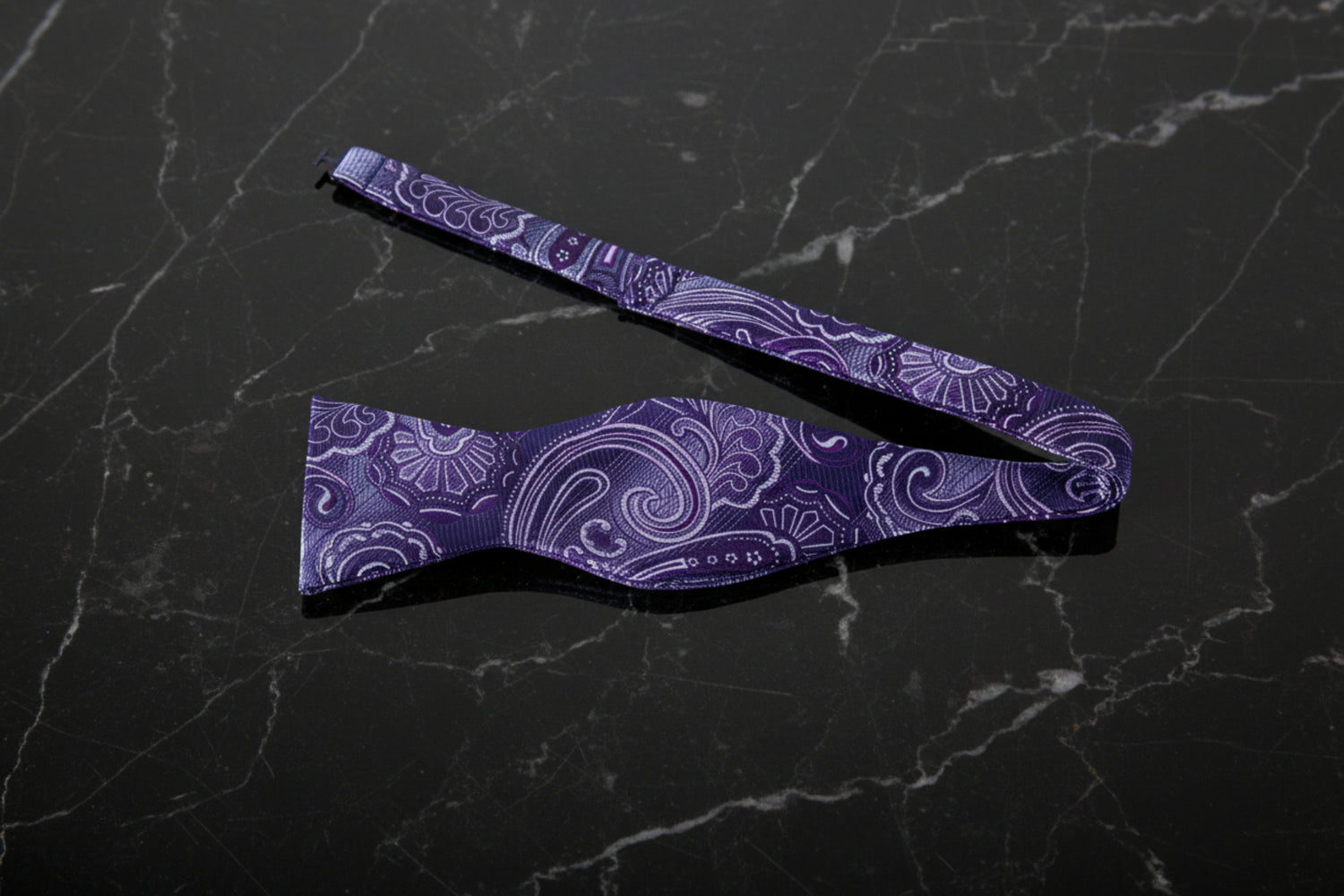 A steel purple and grey paisley bow tie with a matching pocket square, displayed on a white background.